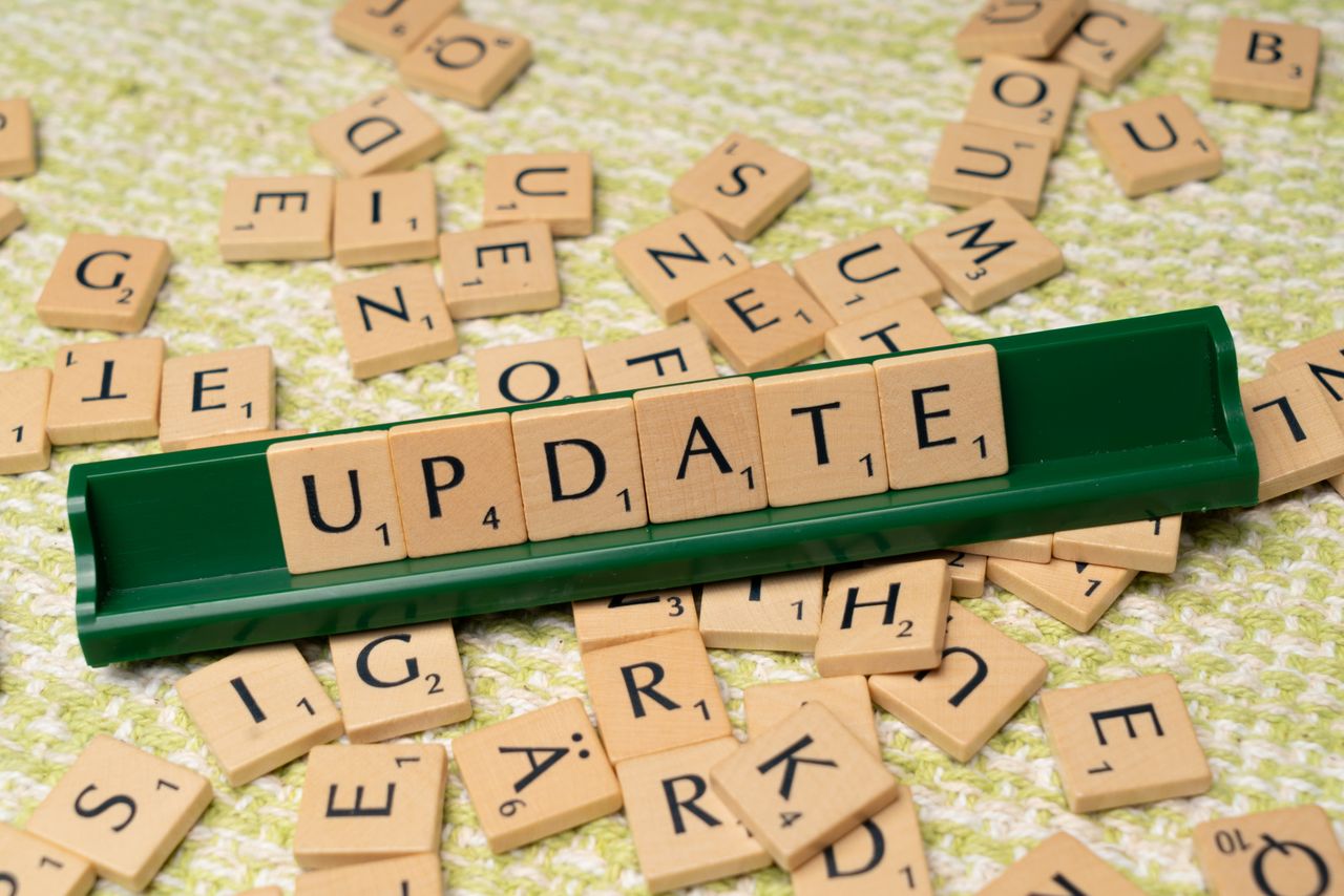 Wooden Scrabble tiles spelling 'UPDATE' with scattered tiles on a textured surface.