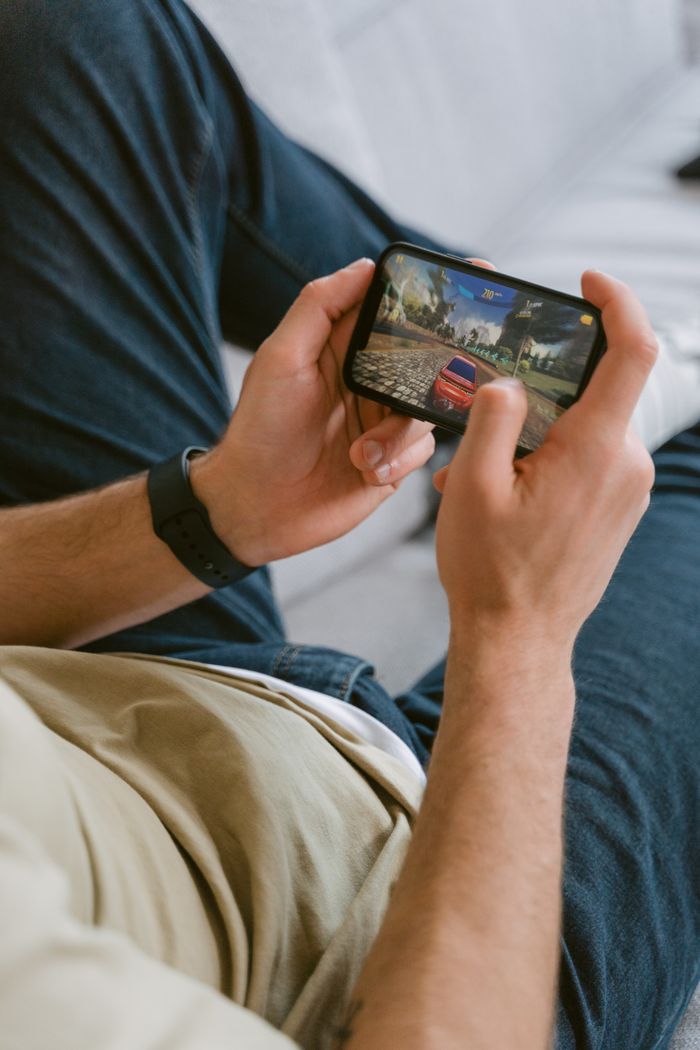 A young adult playing a racing game on a smartphone indoors, focused and relaxed.